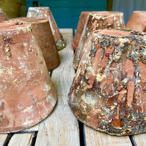 Op de afbeelding: Een verzameling terracotta potten met een rustieke, verweerde afwerking. De potten zijn gerangschikt op een houten oppervlak en hebben een natuurlijke, aardse tint.