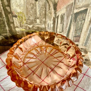 May include: A vintage pink glass ashtray with a scalloped edge and a starburst pattern in the centre.