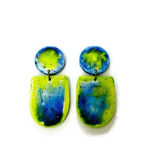 May include: A pair of dangle earrings with a green and blue abstract design. The earrings are made of polymer clay and have a glossy finish.