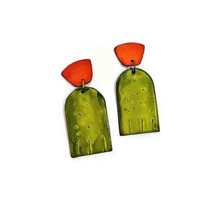 May include: A pair of green and orange geometric ceramic earrings. The earrings are shaped like arches with a small orange triangle on top.