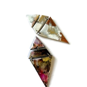 May include: Abstract geometric earrings. Each earring is composed of three connected triangular segments. The segments feature a mix of colors, including white, gold, brown, and pink, with a marbled effect. The earrings are connected with small metal rings.