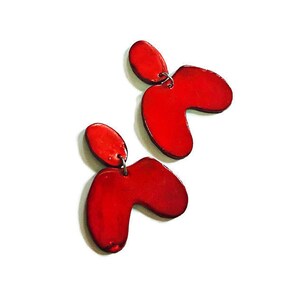 Peut inclure: Une paire de boucles d'oreilles de forme abstraite rouge. Les boucles d'oreilles sont en céramique et ont une finition brillante.