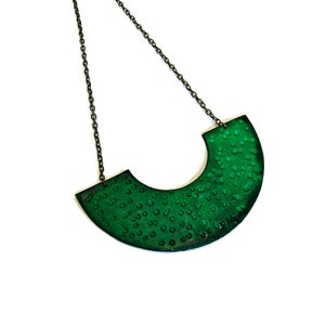 May include: A green statement necklace with a textured, semi-circular pendant. The pendant has a dotted pattern and is attached to a silver chain.