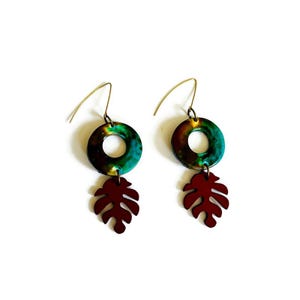 May include: A pair of dangle earrings with a green, brown and gold ring and a maroon leaf charm.