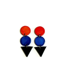 May include: A pair of colourful geometric earrings. Each earring features a red circle, a blue circle, and a black triangle. The earrings are suspended from small metal loops.