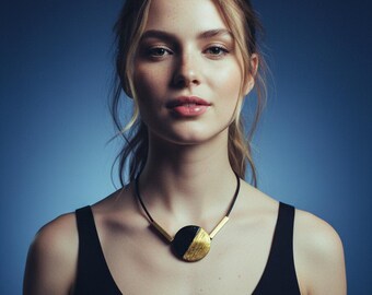 May include: A black and gold necklace with a circular pendant. The pendant is split, with one half gold and the other black. The necklace has a black cord and gold bars extending from the pendant. The woman is wearing a black tank top.