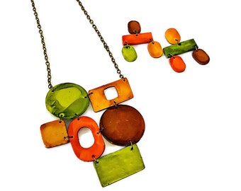 May include: A colorful necklace and matching earrings set. The necklace features a chain with various geometric shapes in shades of green, orange, and brown. The earrings have a similar design. The jewelry is set against a white background.