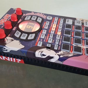 Könnte beinhalten: Eine schwarze und rote elektronische Drum Machine mit einem benutzerdefinierten Anime-Design. Die Drum Machine hat ein großes Display mit der Nummer 18. Das Design zeigt einen japanischen Spruch "NANI!?" und Anime-Charaktere.