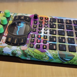 May include: A black and green music sampler with a Dragon Ball Z themed design. The sampler has a large display screen, multiple buttons, and knobs. The text "SP-404-SX" is printed on the side of the sampler.