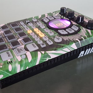 May include: A green and white tropical leaf patterned drum machine with a black base and the text "ADDICT" on the side. The drum machine has a digital display with the text "055CHOT ULTRA 320" on the top right corner.