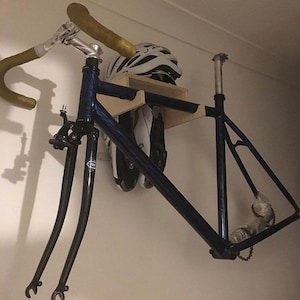 May include: A blue bicycle frame is mounted on a wooden wall rack with a white helmet and black and white rollerblades. The bicycle has a black handlebar and a black fork.