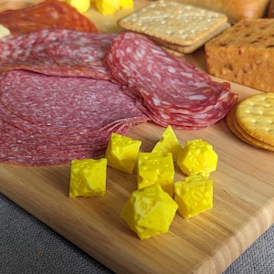 May include: A wooden charcuterie board with a selection of food. Sliced salami, crackers, and yellow cheese cubes are arranged on the board. Other items include cheese blocks and a red meat.