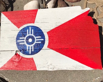 May include: A wooden sign painted with the flag of the city of Albuquerque, New Mexico. The flag features a red, white, and blue color scheme with a stylized sun symbol in the center.