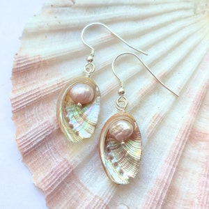 May include: A pair of silver earrings with a pink pearl and iridescent seashell charm.