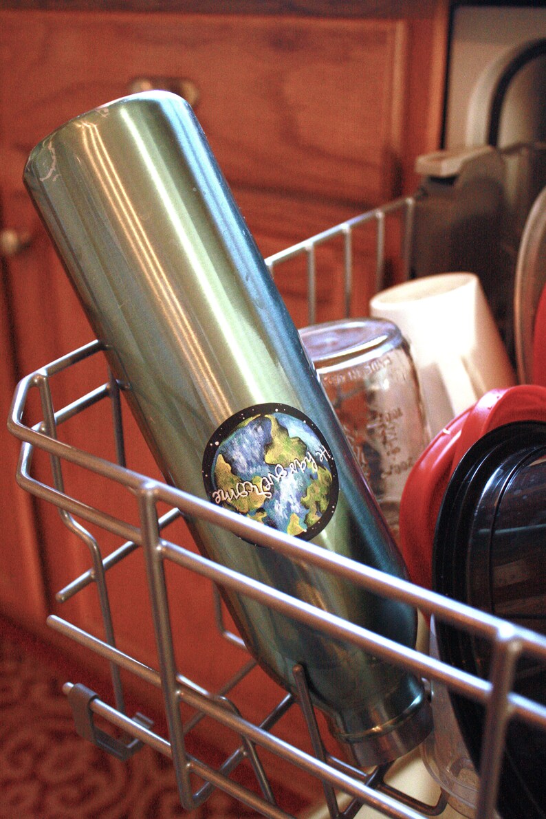 May include: A stainless steel water bottle with a blue and green earth sticker that says "Our Earth, Our Home". The bottle is in a dishwasher rack.