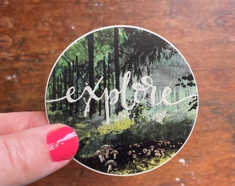 Könnte beinhalten: Ein runder Aufkleber mit einem Aquarellbild einer Waldszene. Der Text "explore" ist in weißer Kursivschrift über dem Wald geschrieben. Im Vordergrund befinden sich Pilze.