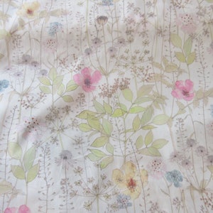 May include: A white fabric with a delicate floral pattern. The flowers are in shades of pink, yellow, and blue, and the leaves are a light green. The fabric has a soft, textured feel.