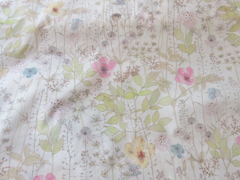 May include: A white fabric with a delicate floral pattern. The flowers are in shades of pink, yellow, and blue, and the leaves are a light green. The fabric has a soft, textured feel.