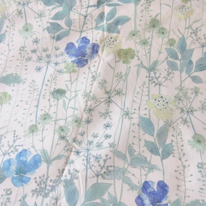 May include: A white fabric with a blue and green floral pattern. The flowers are stylized and resemble watercolor paintings. The fabric has a subtle texture.