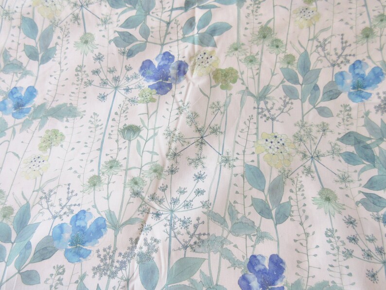 May include: A white fabric with a blue and green floral pattern. The flowers are stylized and resemble watercolor paintings. The fabric has a subtle texture.