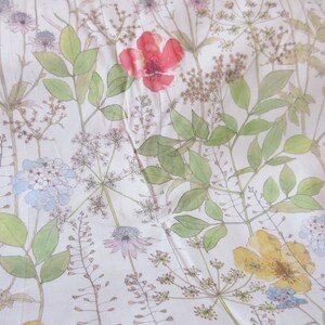 May include: A white fabric with a floral pattern. The pattern features various flowers, leaves, and stems in shades of green, blue, yellow, and red. The background is a light cream color.