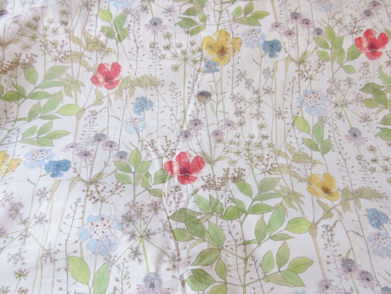 May include: A white fabric with a floral pattern featuring red, yellow, and blue flowers. The flowers are scattered throughout the fabric and are surrounded by green leaves.