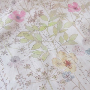 May include: A white fabric with a floral pattern featuring pink, yellow, and blue flowers. The flowers are surrounded by green leaves and stems.