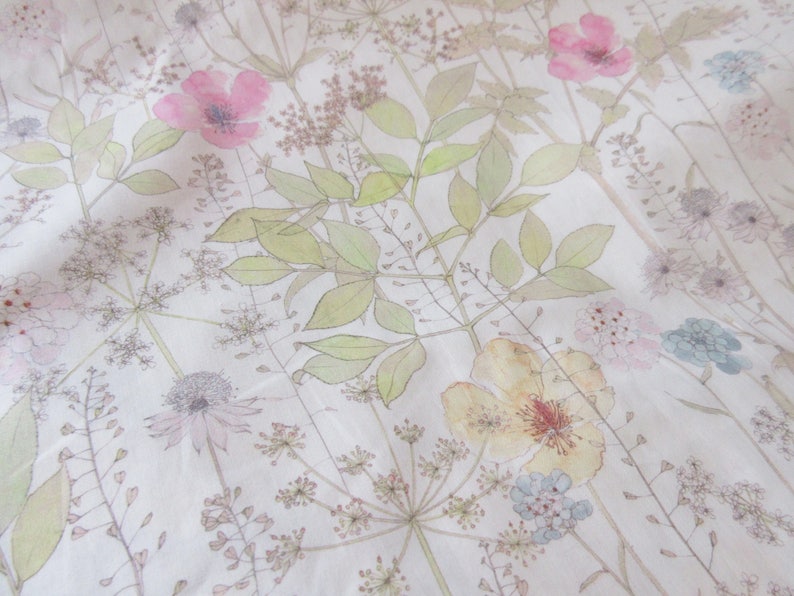 May include: A white fabric with a floral pattern featuring pink, yellow, and blue flowers. The flowers are surrounded by green leaves and stems.