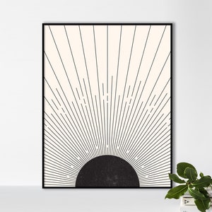May include: A framed art print featuring a minimalist sunburst design. The artwork has a black semi-circle at the bottom, with black lines radiating upwards against a cream-colored background. The frame is black.