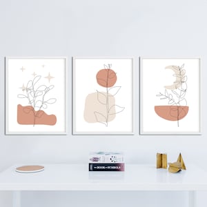 May include: Three minimalist line art prints with a white background and a single plant in each. The first print features a plant with a pink and beige background and stars. The second print features a plant with a beige and orange background. The third print features a plant with a pink and beige background and a crescent moon.