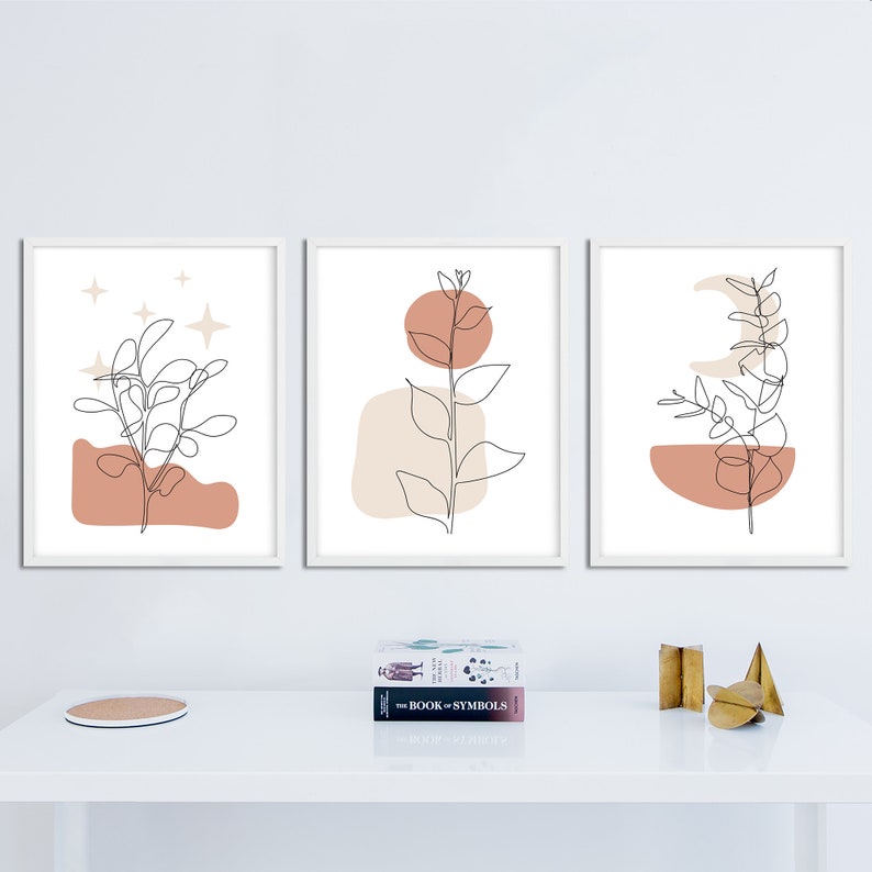 May include: Three minimalist line art prints with a white background and a single plant in each. The first print features a plant with a pink and beige background and stars. The second print features a plant with a beige and orange background. The third print features a plant with a pink and beige background and a crescent moon.