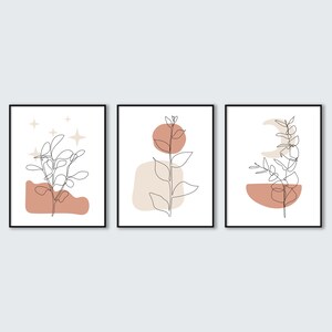 May include: Three minimalist line art prints with abstract shapes and foliage in shades of brown and beige. The prints are framed in black.