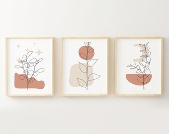 May include: Set of three minimalist line art prints featuring abstract shapes and foliage in shades of brown, beige, and white. The prints are framed in natural wood.