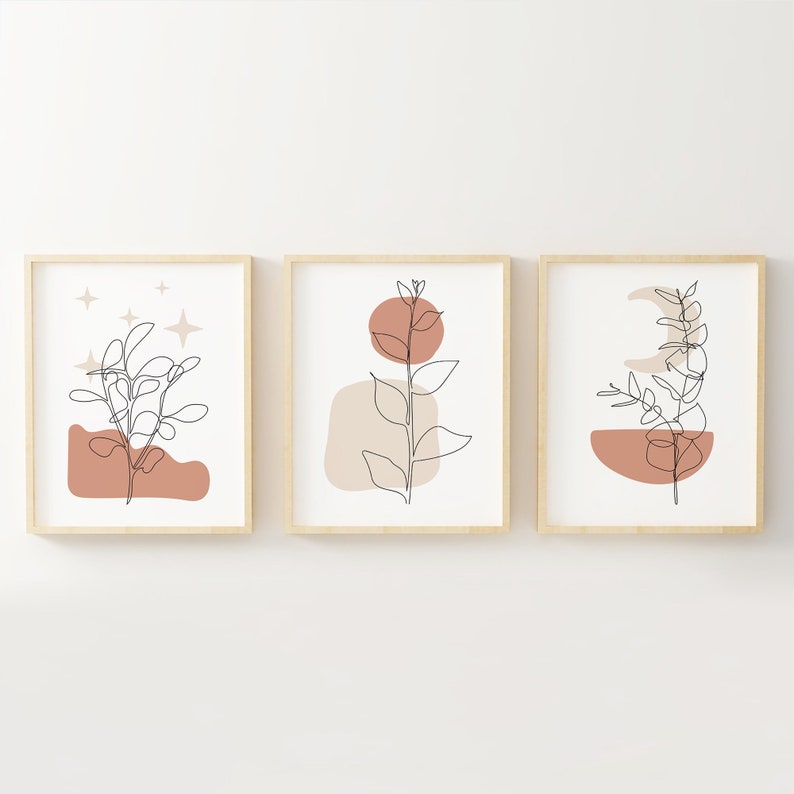 May include: Set of three minimalist line art prints featuring abstract shapes and foliage in shades of brown, beige, and white. The prints are framed in natural wood.