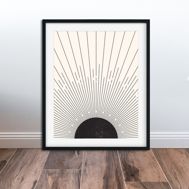 May include: Framed art print featuring a minimalist sunburst design. The artwork has a black semi-circle at the bottom, with black lines radiating upwards against a cream-colored background. The print is encased in a black frame, suitable for wall decor.