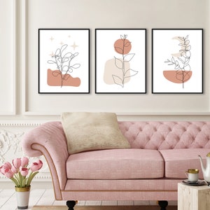 May include: Set of three minimalist line art prints featuring abstract shapes and botanical illustrations in shades of brown and beige. The prints are framed in black and displayed on a white wall.