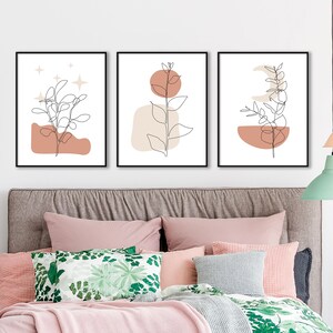 May include: Set of three minimalist line art prints featuring a branch with leaves, a crescent moon, and a sun. Each print has a peach and beige abstract shape behind the branch. The prints are framed in black.