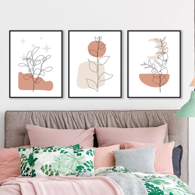 May include: Set of three minimalist line art prints featuring a branch with leaves, a crescent moon, and a sun. Each print has a peach and beige abstract shape behind the branch. The prints are framed in black.
