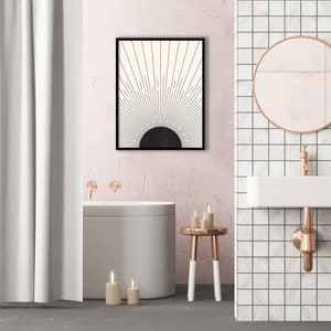May include: A framed abstract art print featuring a black and white sunburst design. The artwork hangs above a modern bathtub in a bathroom setting. The bathroom has a pink wall, a white sink, and a round mirror.