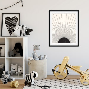 May include: A framed black and white abstract art print depicting a sunburst design. The room also features a white shelf with toys, a wooden tricycle, and a star-patterned rug.