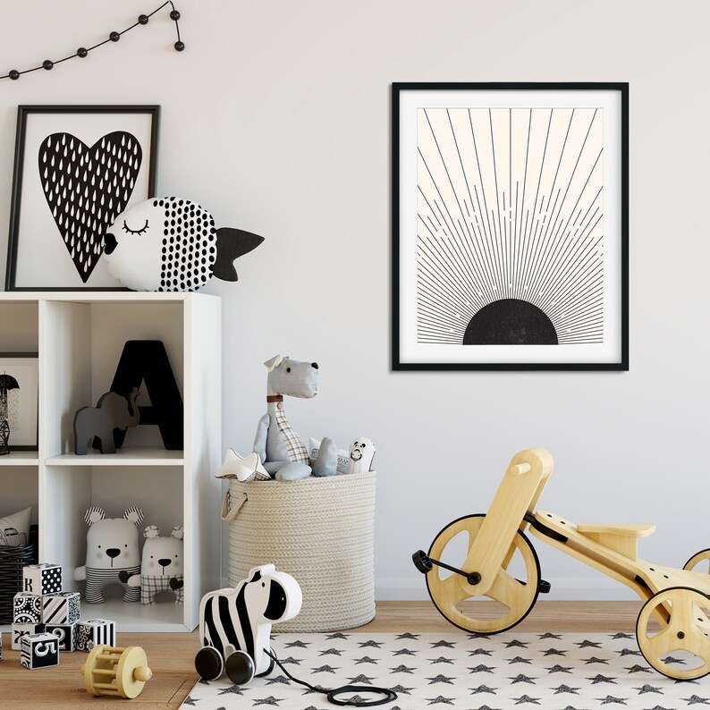 May include: A framed black and white abstract art print depicting a sunburst design. The room also features a white shelf with toys, a wooden tricycle, and a star-patterned rug.