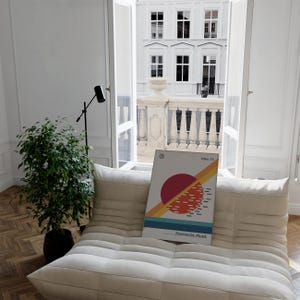 May include: A white, tufted sofa with a poster featuring a red sun and colorful stripes. The poster reads "Köln 73" and "Kosmische Musik." A black lamp and a potted green plant are also visible.