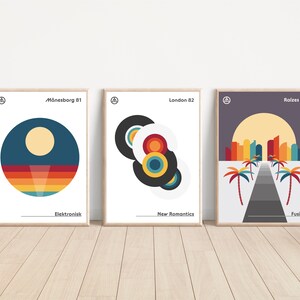 May include: Three framed posters with geometric designs and text. The first poster is blue, yellow, and orange with the text "Mönnesborg 81" and "Elektronisk". The second poster is white with black, red, yellow, and blue circles and the text "London 82" and "New Romantics". The third poster is purple with yellow, orange, and red buildings and palm trees and the text "Raizes 85" and "Fusion".