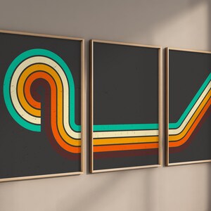 May include: A triptych of framed art prints with a retro design. Each print has a dark grey background with colourful curved lines in teal, yellow, orange, and brown. The frames are a light wood colour.