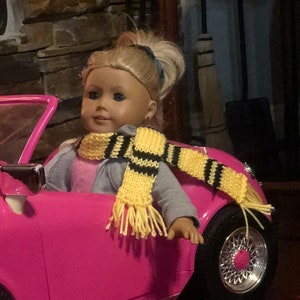 May include: A pink toy car with a doll wearing a yellow and black striped scarf. Four scarves in the colors of Gryffindor, Slytherin, Ravenclaw, and Hufflepuff are laid out on the floor.