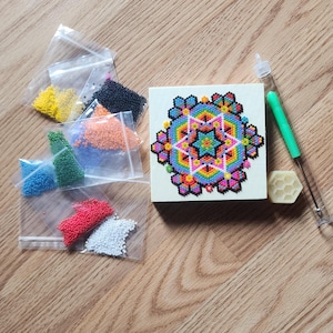 Peut inclure: Un kit de mandala en perles colorées avec une base en bois, une aiguille, un bloc de cire et des sachets de perles de différentes couleurs, notamment jaune, orange, rouge, bleu, vert, noir et blanc.