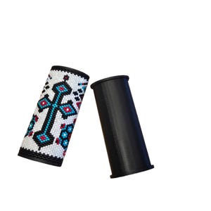 May include: Two black and white beaded seat belt covers. One cover features a turquoise cross design with red and blue accents. The other cover is solid black.