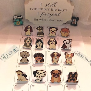 May include: A collection of twenty small, colorful dog-themed charms arranged in a grid on a white sheet. Each charm features a different dog breed illustration. A wooden sign at the top reads, I still remember the days I prayed for what I have now.