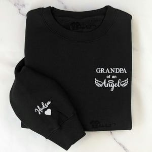 May include: Black sweatshirt with white text that reads "Grandpa of an Angel" with angel wings. The left sleeve has the name "Hudson" and a small heart.