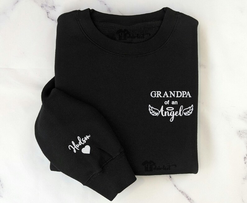 May include: Black sweatshirt with white text that reads "Grandpa of an Angel" with angel wings. The left sleeve has the name "Hudson" and a small heart.